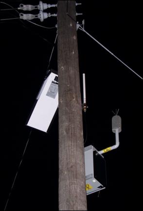 A permanently mounted automated wireless noise monitoring system is attached to the top of a telephone pole. Note the solar cell for power, an antenna and transmitter for sending data, and a microphone covered with a cylindrical windscreen. 