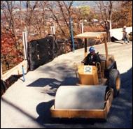 Several construction workers use a typical soil compacter on a roadway project. In comparison, the picture on the left is of the same roadway project with several construction workers using a vibratory soil compacter, which is much smaller in size.