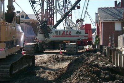 Many pieces of equipment, such as cranes and excavators, are operating on a construction site less than five feet from adjacent businesses and residences.