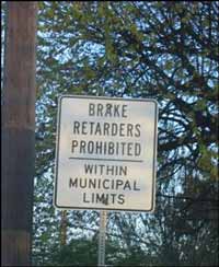 An informational street sign (white background with black letters) declaring brake retarders (engine compression brakes) are prohibited within municipal limits.