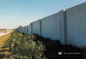 photo:  precast concrete noise barrier, with good shrub-type landscaping in front of the barrier, and a highway with traffic (photo is intended to illustrate a typical example of a wall-type noise barrier)
