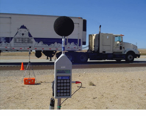 This figure contains 3 photographs of noise measurement set-ups that are in conformance with the set-up required for REMEL level measurements. The first contain two individuals setting up a radar gun to determine the speed of the traffic.  The second is of an individual setting up a video camera to tape the traffic as measurements are being taken.  The third is of two noise meter as different distances from the road, while a heavy truck passes by. 