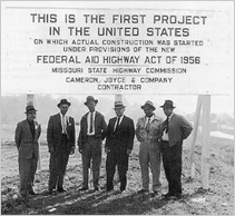 Title: First Project under Federal Aid Highway Act of 1956 - Description: A group of six men standing in front of a large sign at the site of the first transportation project under the Federal Aid Highway Act of 1956.