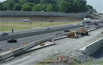 Title: Highway Under Construction - Description: A bird's eye view of a multi-lane highway under construction with an adjacent noise barrier.