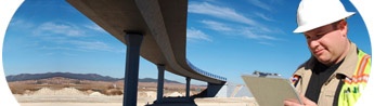 Construction worker standing by highway overpass with a clipboard.