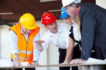 Business people wearing hard hats looking at plans on a construction site.