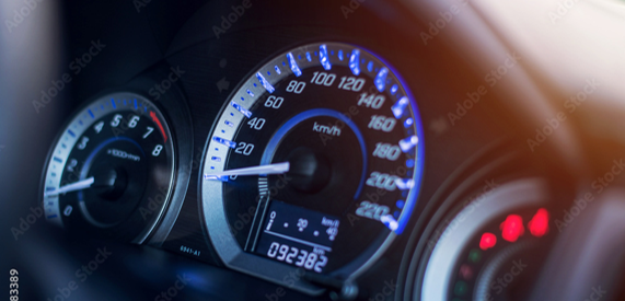 Car dashboard with illuminated instruments, including a prominent speedometer displaying the current speed.