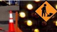 Highway construction work  -  zone is shown with orange - and - white cone on left and black-on-gold diamond-shaped sign showing construction person at work.