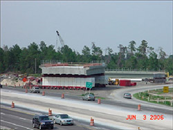 A new bridge span supported by self-propelled modular transporters is shown in a staging area where the span was constructed near the bridge location.