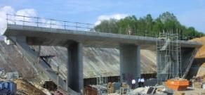 A completed concrete bridge constructed adjacent to an existing railroad embankment waiting to be launched transversely into place.