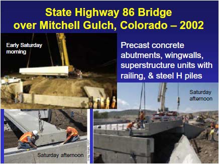 Mitchell Gulch Bridge during weekend construction. The upper portion of the precast concrete abutment has been lifted by a crane and is being moved into position above the lower portion of the abutment that is already in place. The precast concrete wingwall on the left is in position and the wingwall to the right is lying near its final position. Construction workers are assisting with the erection.