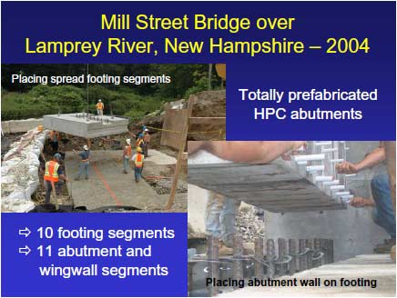 Mill Street Bridge during construction. Construction workers are erecting the spread footing foundation at an abutment. The first spread footing segment has been lifted by a crane and is being moved into position above the prepared surface.