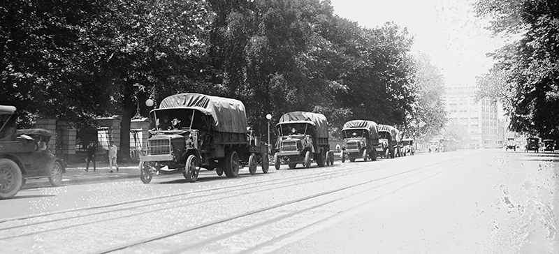 Black and white photograph of the Transcontinental Convoy making its way though a city.