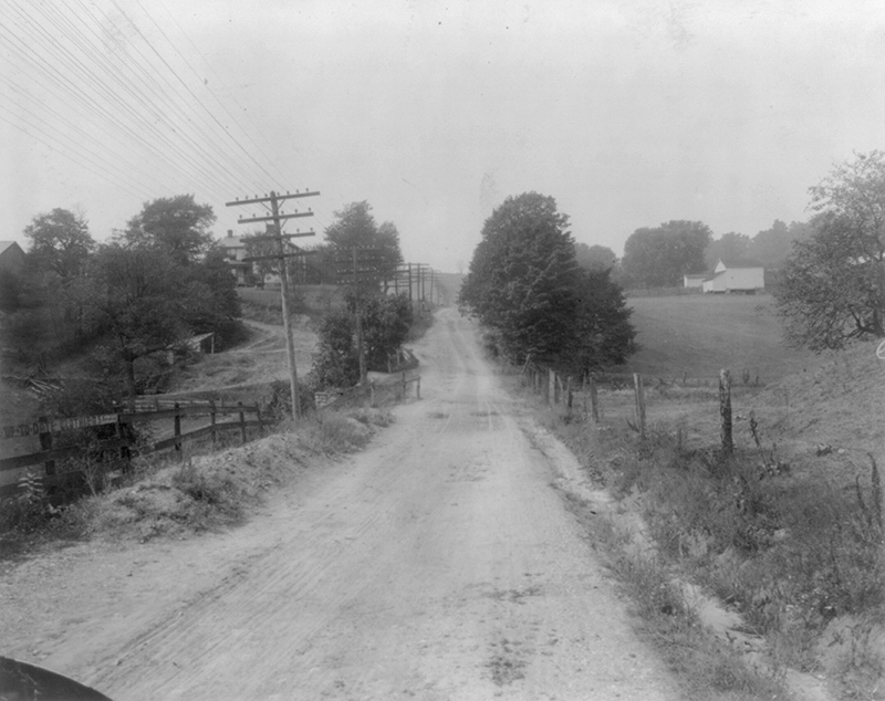Black and white photograph looking down The Cumberland road. It is a dirt road with no traffic.