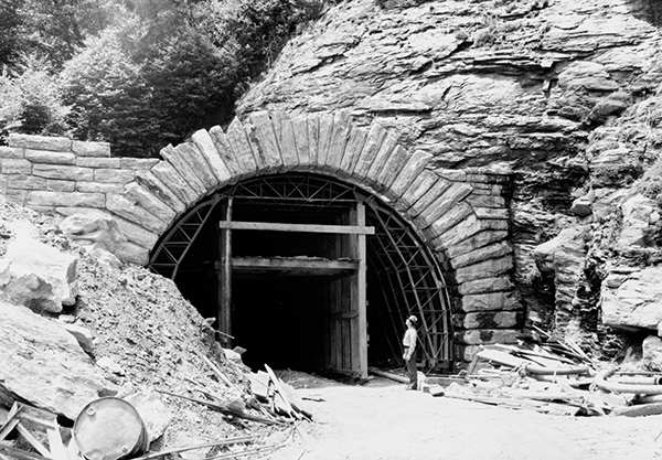 Black and white photograph showing a man standing in the opening of a tunnel in the first section of the Blue Ridge Parkway.