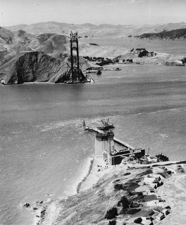 Black and white aerial photograph of the Golden Gate Bridge in its early stages of construction.