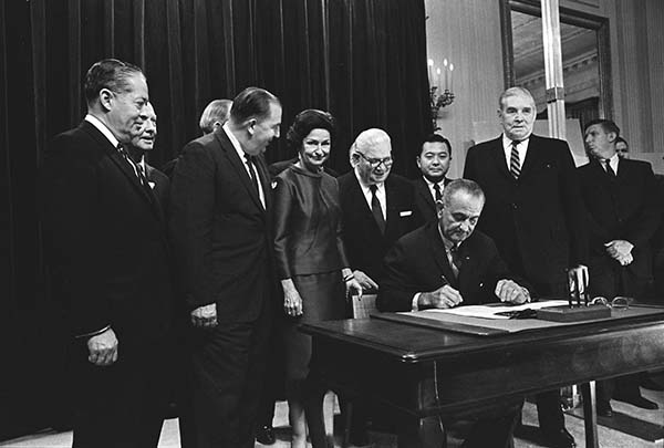 Black and white commemorative photograph of President Johnson signing the Highway Beautification Act in the Oval Office.