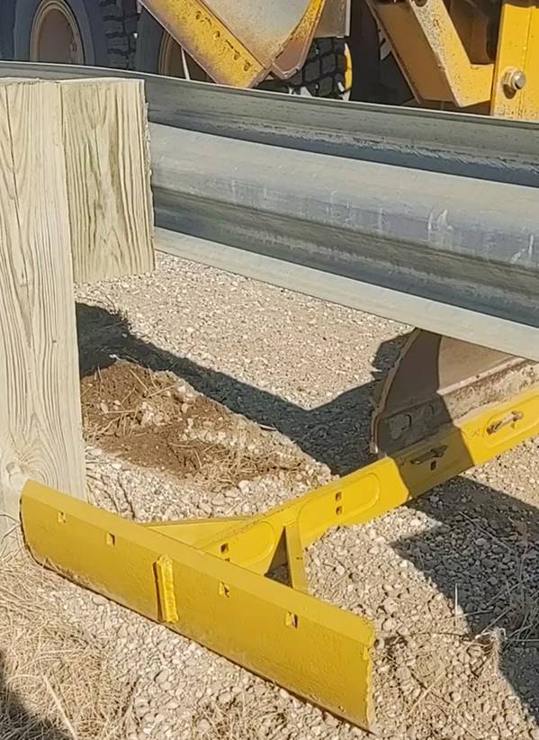 Guardrail maintainer cleaning debris from around a guard rail.