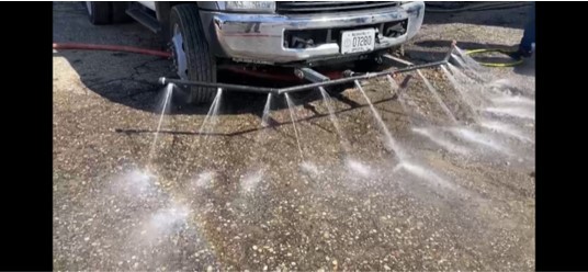 A car on a dirt road with water sprayer attachment on front bumper