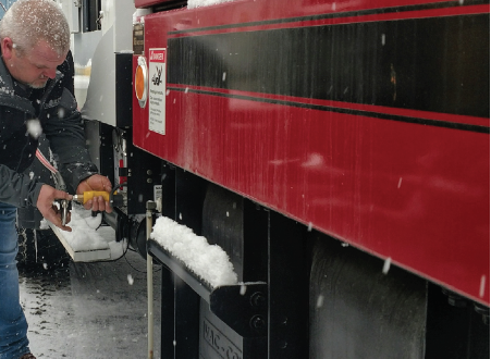 Image shows a man working on the side of a commercial truck with the service panel open.