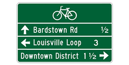 This figure shows a horizontal rectangle green sign with a white legend and border and three white horizontal dividers.  On the top line is a bicycle symbol.  On the second line is a up through arrow with the legend "Bardstown Rd ½" .  The third line is a left arrow with the legend "Louisville Loop 3".  The bottom line has the legend "Downtown District ½" with a right arrow.