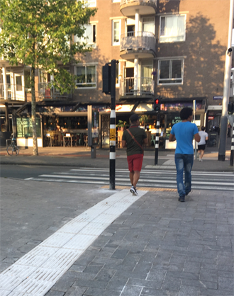 Photo of a directional indicator leading to a crosswalk. A pedestrian is walking on top of the directional indicator toward the crosswalk.