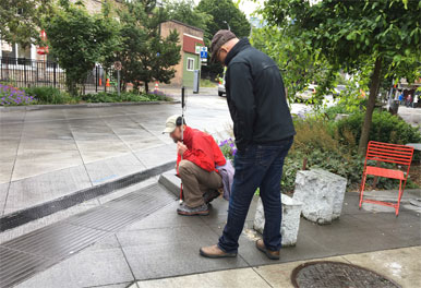 Photo of two men standing at the edge of a shared street who appear to assessing how well that edge functions for pedestrians with vision disabilities.