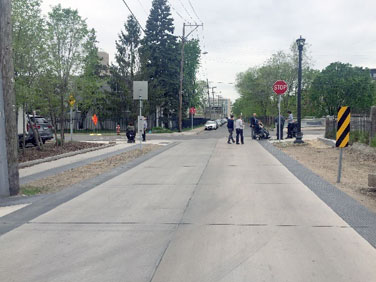 Photo of a shared street on which the shared zone appears to be made of standard, light gray concrete of the type that you commonly see on conventional streets.