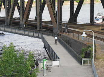 Photo of a person riding a bicycle on a path adjacent to a bridge.
