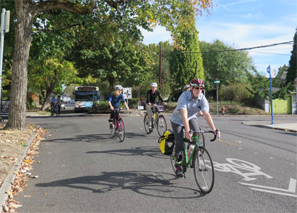 A group of cyclist riding their bikes on a road with bike lane pavement markings, indicating a shared bike and car facility.
