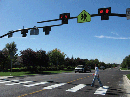 Image is of traffic signals and a crosswalk with a person crossing a busy highway.