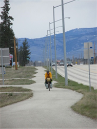 Image is of a bicyclist on a bikeway beside a busy roadway.