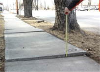 Image shows an assessment participant measuring uneven sidewalk.