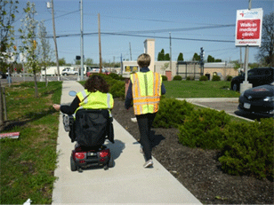 Image shows assessments participants, one of whom is in a wheelchair, walking on a sidewalk.