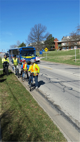 Image shows assessment participants on bicycles, on a narrow roadway with a bus.