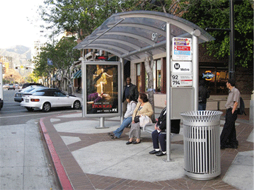 Image shows bus shelter with travelers waiting for a bus.