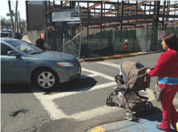 Image is of a woman and a stroller in a crosswalk, with a car turning into the crosswalk.