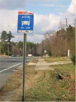 Photo of a bus stop sign and sidewalk that stops short or bus stop.
