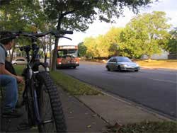 Photo of bicyclist on sidewalk waiting for approaching bus.
