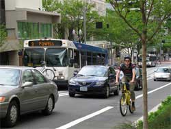 Photo of bicyclist on left side of urban road traveling with flow of traffic.