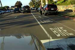 Photo of bicyclist riding in bike lane close to parked cars.