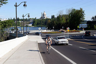Photo of a bicyclist riding on shoulder of roadway after roundabout and bridge.