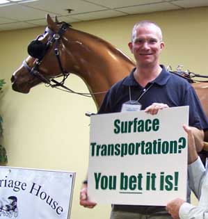 Photo of Christopher standing next to a lifesize model horse and holding a sign that says 'Surface Transportation? You bet it is!'
