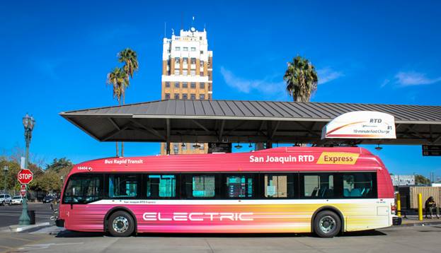 An electric bus is parked outside of a bus stop.