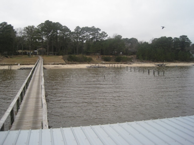 View down a wooden pier back towards the shore shows the water and pocket beaches.