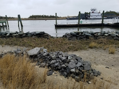 Large pile of rocks in the foreground and a large line of rocks with a gap in the background at the edge of the water.