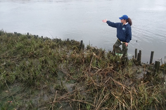 Tour leader extends arm to show the native plants on a slope next to a waterway.