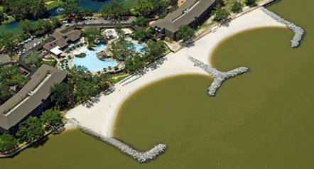 Aerial photograph of two pocket beaches stretching into the water to protect a development with large buildings and a pool. The rocky headland structures are situated perpendicular to the beaches, with parallel arms further into the water to create a protective buffer.