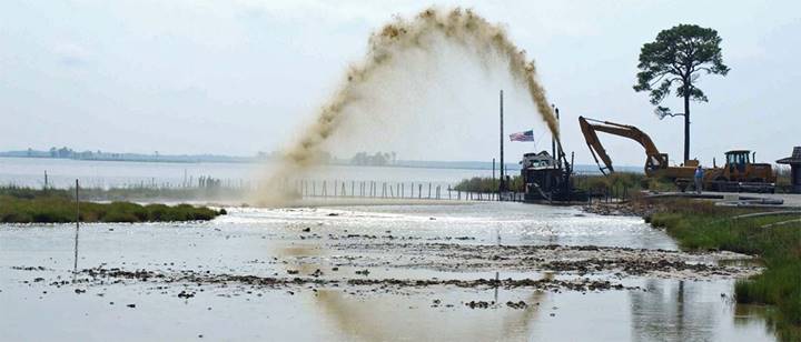 Photograph of a dredge spraying a slurry of sediment and water over a tidal marsh.