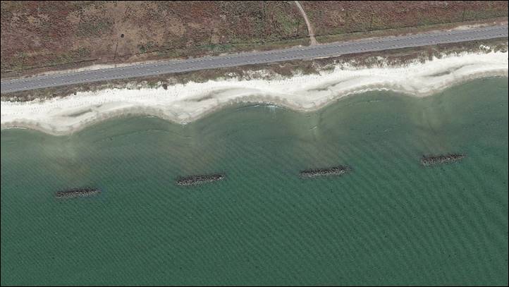 Aerial photograph showing offshore segmented rock breakwaters stabilizing a sandy shoreline that protects a coastal highway in Louisiana.